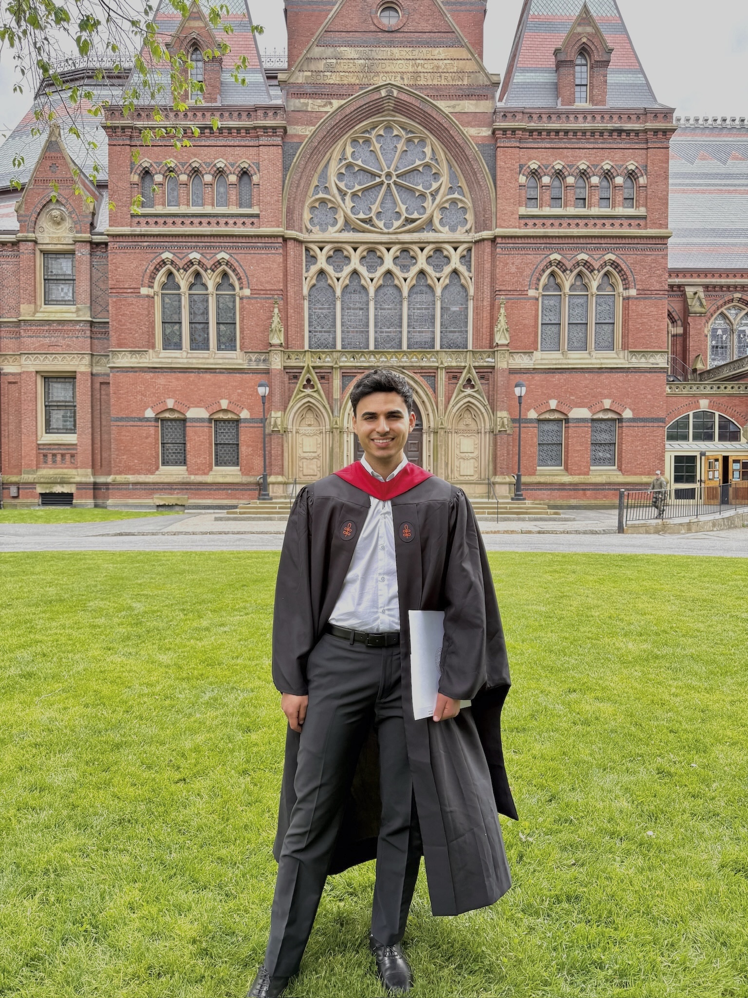 Essam Sleiman in graduation robes in front of a brick campus building